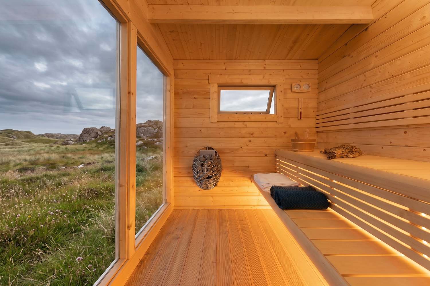 Inside the sauna: pine benches, a basket heater and a full-height window onto the machair